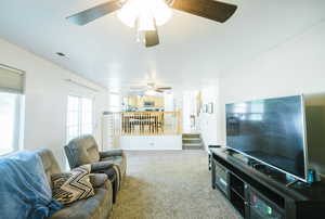 Living room with a ceiling fan, carpet floors, and stairway