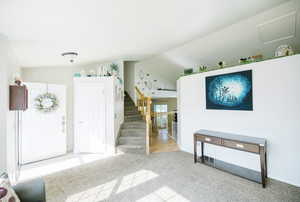 Foyer featuring lofted ceiling, carpet floors, stairs, and baseboards