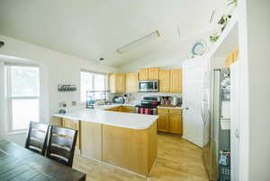 Kitchen with stainless steel appliances, a peninsula, a sink, vaulted ceiling, and light countertops