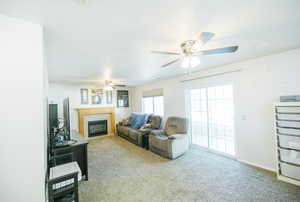 Living area with ceiling fan, carpet, a tiled fireplace, and baseboards