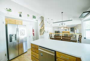 Kitchen with appliances with stainless steel finishes, light wood-style flooring, light countertops, pendant lighting, and a chandelier