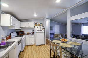 Kitchen featuring white appliances, vaulted ceiling, light wood finished floors, white cabinetry, and light countertops