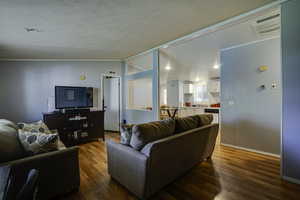 Living area with wood finished floors, a textured ceiling, vaulted ceiling, and crown molding