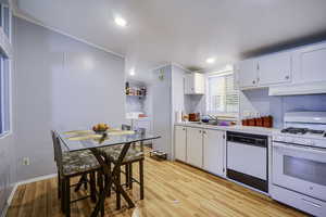 Kitchen featuring white appliances, under cabinet range hood, light countertops, light wood-style flooring, and a sink