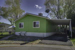 View of property exterior with asphalt driveway, a carport, fence, and central AC