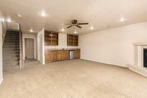 Unfurnished living room with wet bar, baseboards, light carpet, recessed lighting, and stairs