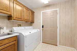 Laundry area with wallpapered walls, washer and dryer, cabinet space, a textured ceiling, and baseboards