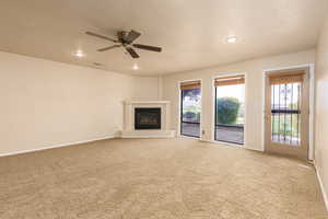 Unfurnished living room with carpet, a textured ceiling, a glass covered fireplace, plenty of natural light, and recessed lighting