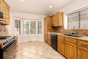 Kitchen with dishwasher, electric stove, a sink, tasteful backsplash, and light stone countertops
