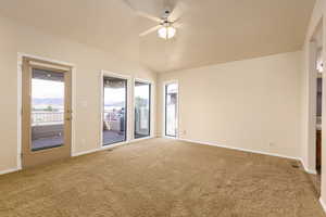 Carpeted spare room featuring a ceiling fan, vaulted ceiling, and baseboards