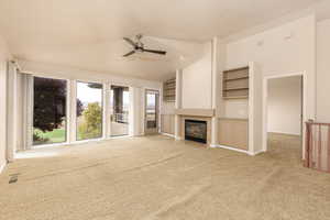 Unfurnished living room featuring carpet flooring, a ceiling fan, a tiled fireplace, and lofted ceiling