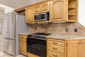 Kitchen with appliances with stainless steel finishes, backsplash, light stone countertops, and light tile patterned floors