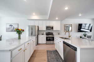 Kitchen featuring stainless steel appliances, a center island with sink, a sink, recessed lighting, and light wood-style flooring