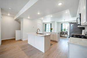 Kitchen featuring a sink, a center island with sink, stainless steel microwave, light wood finished floors, and recessed lighting