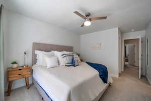 Primary bedroom with light colored carpet, baseboards, and a ceiling fan