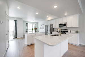Kitchen featuring appliances with stainless steel finishes, a kitchen island with sink, a sink, baseboards, and recessed lighting