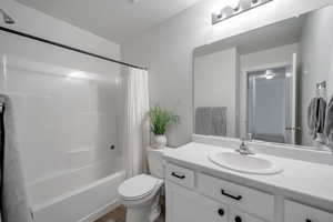 Bathroom featuring wood finished floors, a textured ceiling, toilet, vanity, and shower / tub combo with curtain