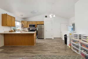 Kitchen featuring appliances with stainless steel finishes, a peninsula, lofted ceiling, wood finished floors, and light countertops