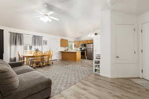 Living room with lofted ceiling, a ceiling fan, light wood-type flooring, and baseboards
