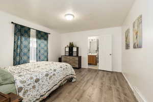 Bedroom with wood finished floors, a textured ceiling, baseboards, and ensuite bathroom