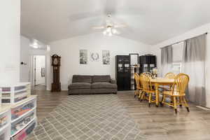 Living room featuring vaulted ceiling, light wood-style flooring, ceiling fan, and baseboards