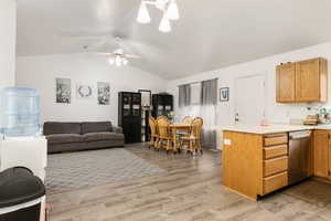 Kitchen with stainless steel dishwasher, vaulted ceiling, light countertops, light wood finished floors, and a peninsula
