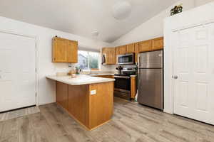 Kitchen with appliances with stainless steel finishes, a peninsula, lofted ceiling, a sink, and light wood-type flooring