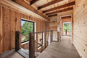 Hallway featuring an upstairs landing, wooden walls, beamed ceiling, and wood ceiling