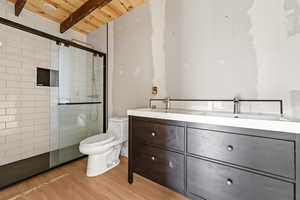 Bathroom featuring wood ceiling, a tile shower, toilet, wood finished floors, and double vanity