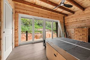 Bedroom featuring wood ceiling, wooden walls, beamed ceiling, multiple windows, and light wood finished floors