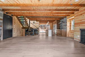 Unfurnished living room featuring wood walls, wood finished floors, wood ceiling, beamed ceiling, and stairs