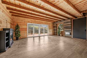 Unfurnished living room featuring beam ceiling, wooden ceiling, wood walls, and light wood finished floors