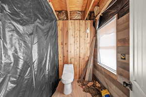 Bathroom with toilet, wood walls, and wood finished floors