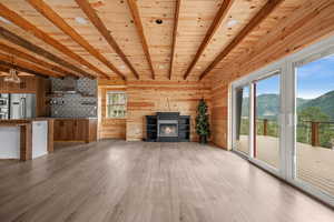 Unfurnished living room with light wood-style flooring, beamed ceiling, a mountain view, wood ceiling, and a glass covered fireplace