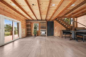 Unfurnished living room featuring wood walls, hardwood / wood-style floors, beamed ceiling, stairway, and wood ceiling