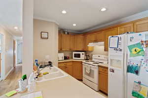 Kitchen featuring white appliances, ornamental molding, a sink, under cabinet range hood, and light countertops