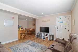 Living area with wood finished floors, crown molding, recessed lighting, and baseboards