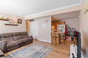 Living room with ornamental molding, light wood-type flooring, recessed lighting, and baseboards