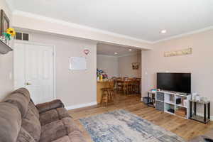 Living area featuring wood finished floors, crown molding, baseboards, and recessed lighting