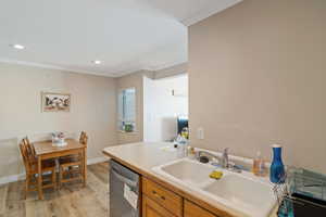 Kitchen featuring stainless steel dishwasher, a sink, ornamental molding, light wood-type flooring, and brown cabinetry