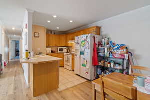 Kitchen with white appliances, crown molding, a peninsula, a sink, and light countertops