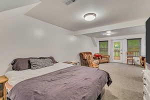 Carpeted bedroom featuring vaulted ceiling, visible vents, and access to exterior