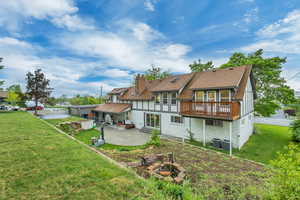 Back of house featuring a patio, a fire pit, a wooden deck, a lawn, and roof with shingles