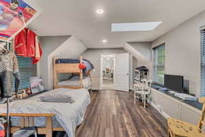 Bedroom featuring wood finished floors, vaulted ceiling with skylight, visible vents, baseboards, and recessed lighting