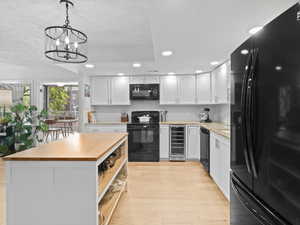 Kitchen featuring black appliances, wine cooler, recessed lighting, white cabinetry, and light wood-style flooring