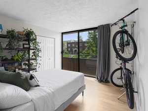 Bedroom with a textured ceiling, light wood-style flooring, access to exterior, a closet, and floor to ceiling windows