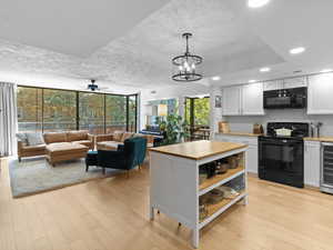 Kitchen with black appliances, light wood-style flooring, white cabinets, wine cooler, and open shelves