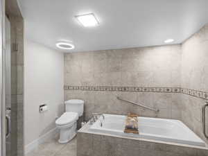 Full bath with toilet, tile patterned floors, a relaxing tiled tub, an enclosed shower, and tile walls