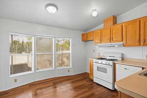 Kitchen with white appliances, under cabinet range hood, light countertops, lofted ceiling, and dark wood-style flooring