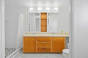 Bathroom featuring toilet, marble finish flooring, a stall shower, and double vanity
